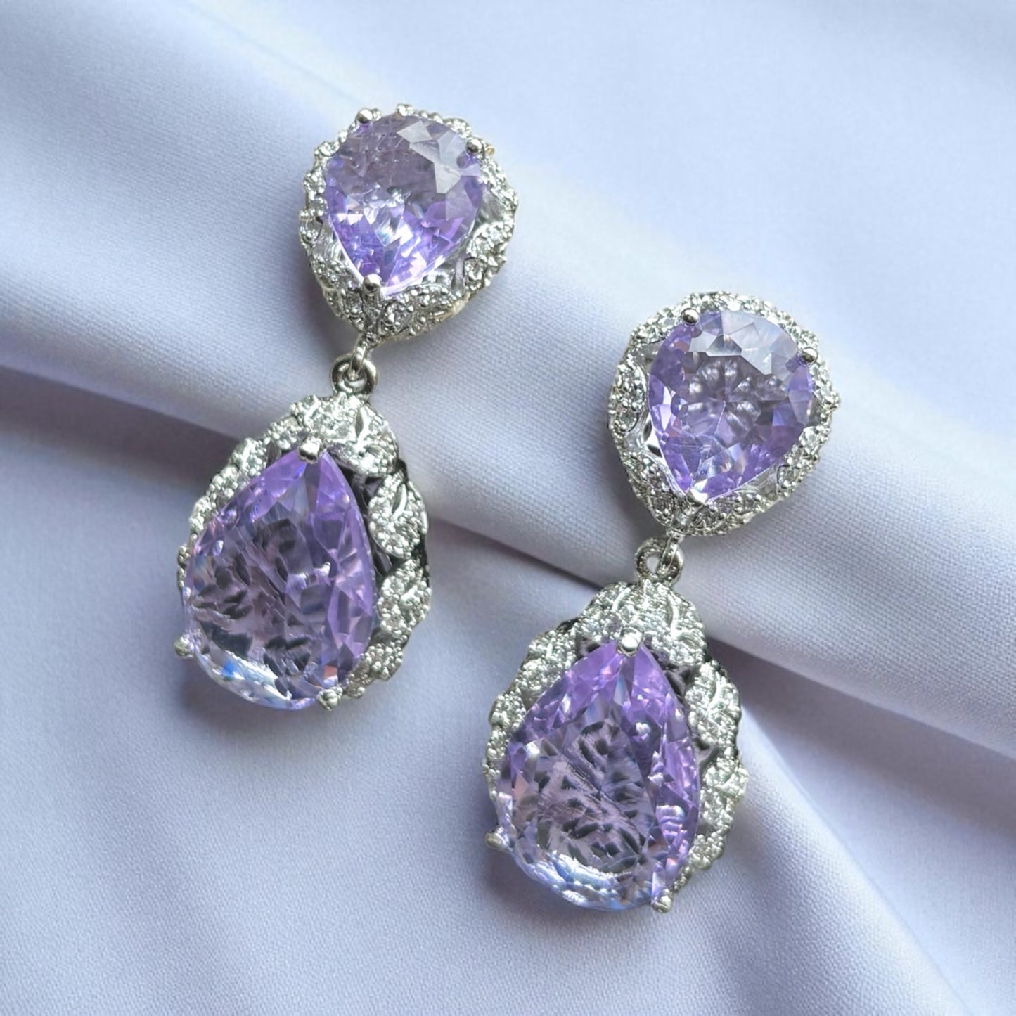 Purple teardrop earrings with silver detailing on a white fabric background