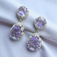 Purple teardrop earrings with silver detailing on a white fabric background