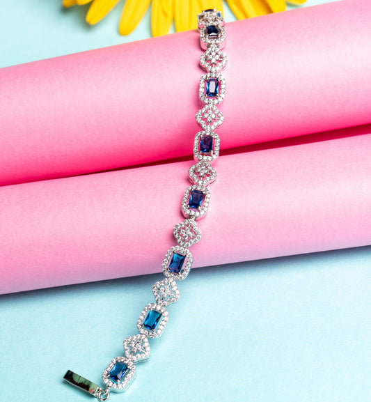 An elegant wristlet bracelet with a multicolored gemstone charm, displayed on a pink background.